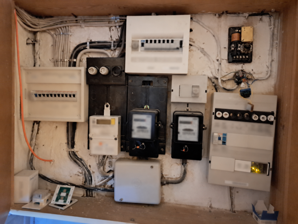 alter Zählerschrank mit mehreren Zählern und alten Sicherungen